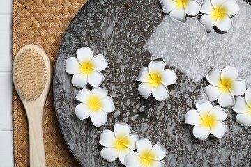Fototapeta na wymiar Bowl of water with plumeria flowers and brush on table, top view. Spa treatment