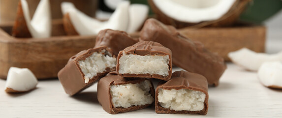 Delicious milk chocolate candy bars with coconut filling on white wooden table, closeup. Banner...