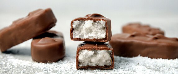 Delicious milk chocolate candy bars with coconut filling on grey table, closeup. Banner design