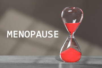 Menopause word and hourglass on table against grey background