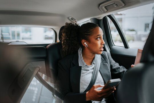 Businesswoman looking through window and talking on smart phone while sitting in car