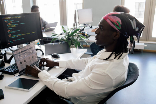 Concentrated male computer programmer working on laptop while sitting at desk in office
