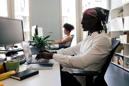 Male computer programmer using laptop while sitting on chair with colleague at office