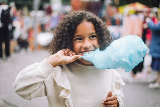 Thoughtful girl eating blue cotton candy at amusement park