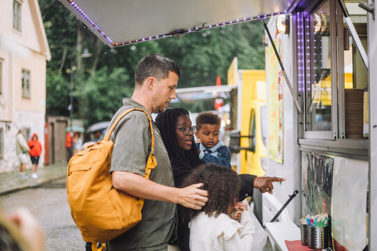 Side view of man standing with family buying snacks from food truck during carnival at amusement park