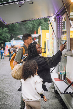 Mother doing contactless payment near food truck while standing with family at amusement park