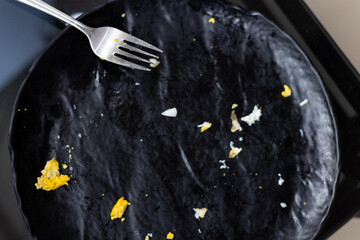 Top view. Black ceramic plate, fork with remains of omelet after breakfast, lunch. Great appetite. 