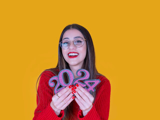 Portrait of young brunette caucasian girl in glasses smiling holding 2024 numbers standing over...