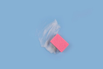 Pink washing Sponge lying on surface in soapy foam on blue background. Cleaning concept,...