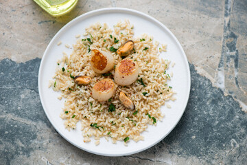 Seared scallops with brown rice and mussels on a white plate, horizontal shot on a grey and beige granite background, elevated view