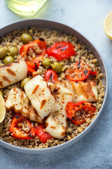 Quinoa salad with grilled halloumi cheese, bell pepper and green olives, vertical shot on a light-blue stone background, middle close-up