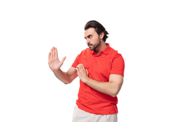 young handsome european brunette man with a beard dressed in a red t-shirt with a mockup actively...