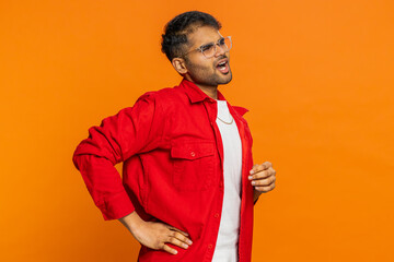 Indian man suffering backache, massaging sore place lower spine, frowning from unbearable spasm torn muscles and tendons, kidney stones pinched nerve. Arabian guy isolated on orange background indoors