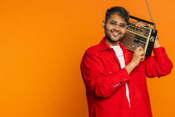 Happy young Indian man using retro tape record player to listen music, disco dancing favorite...