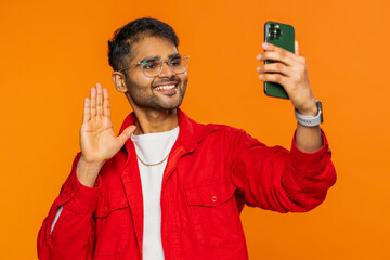 Smiling Indian man blogger taking portrait selfie on smartphone, streaming, vlog, communicating...