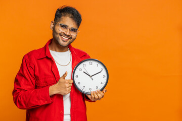 It is your time, hurry up. Indian young man showing time on wall office clock, ok, thumb up approve...