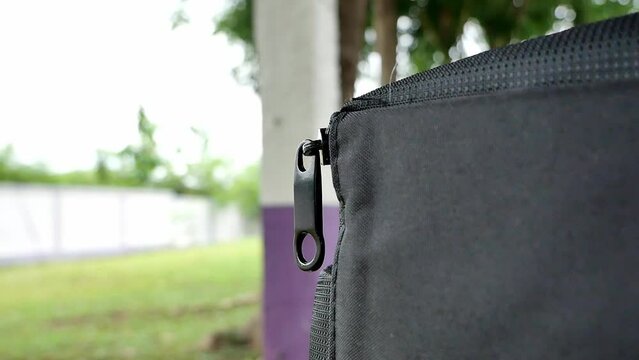 Closeup, A light breeze causes the zipper on the black bag on the table to move slightly. Video macro.