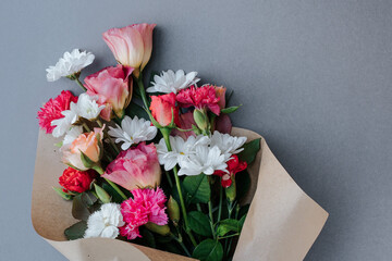 a bouquet of roses, carnations, daisies, eustomes wrapped in paper and lying on a gray background