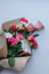 a bouquet of roses, carnations, daisies, eustomes wrapped in paper and lying on a white background
