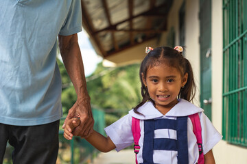 A cute young Filipino girl in a white a blue school uniform, being fetched by her grandfather right after class at a provincial primary school. - obrazy, fototapety, plakaty