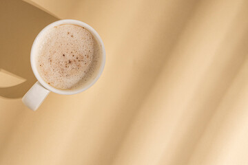 Cappuccino in a white cup with rays of light on a beige background. Flat lay, top view.