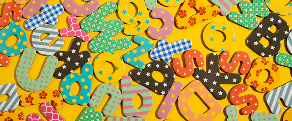 Many multi-colored letters of the alphabet on a yellow background. Top view, flat lay. Banner