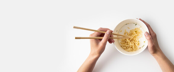 Female hand takes Chinese noodles with Chinese chopsticks from a paper bowl on a white background....