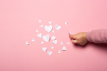Child's hand takes a valentine card from paper on a pink background. Composition Valentine's Day. Banner. Flat lay, top view