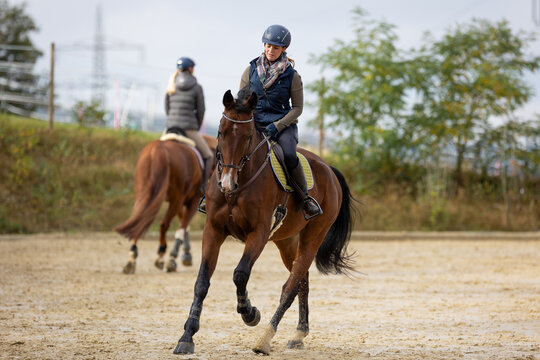Horse during training with rider on the riding arena, galloping in a turn, photographed from the front in the background by another rider.