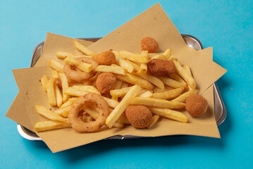 mixed fried food on a metal baking tray with fried potatoes, onions and olives isolated on a blue background
