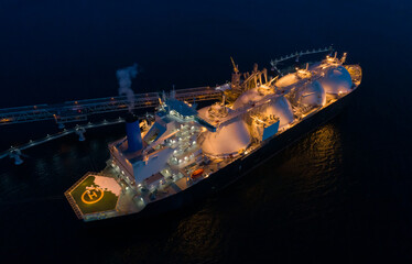 Aerial of Liquified Natural Gas LNG carrier moored to a small gas terminal at dusk. Fuel crisis....