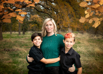 Family of two boys and a mother outdoors together hugging autumn portrait