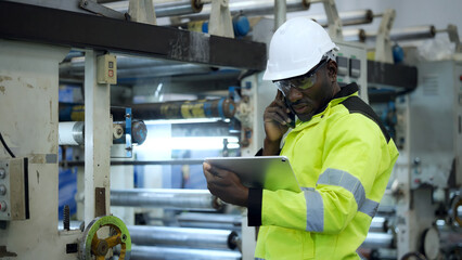 Engineer holding a digital tablet and using phone to communicate with coworkers during inspecting the operation of a plastic machine.