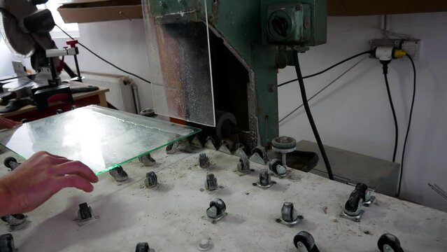 Worker sanding, edging 4 mm thick glass on wet belt sander close up shot.
