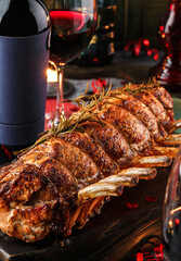 Holiday baked meat tenderloin with ribs, pork, roast beef on dark wooden board with glasses, bottle...