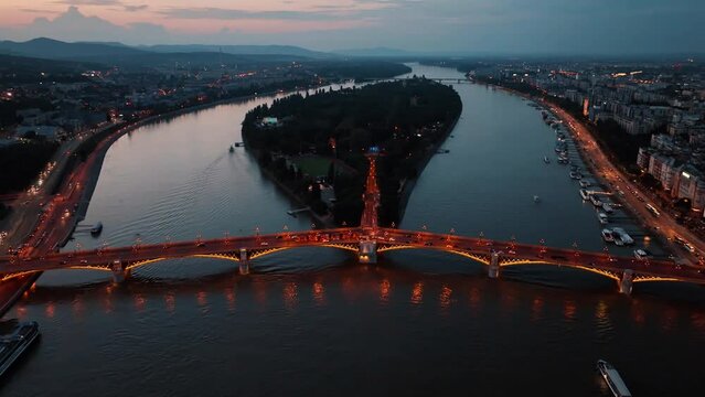 Aerial drone night dolly shot of river cruise ships, bridges illuminated after sunset in Budapest, Hungary