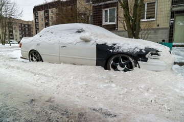 Snowy urban street with a car hidden under snow after snow removal