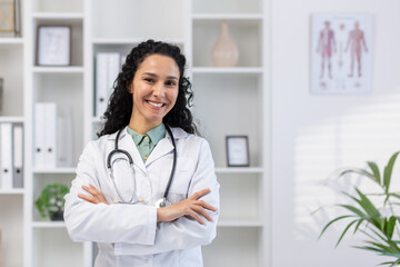 Portrait of young beautiful successful female doctor inside medical office, hispanic woman with...