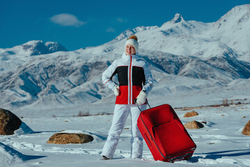 Young woman tourist with red suitcase on winter mountains background