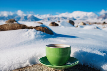 Green teacup in the snow on mountains background in winter