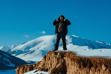 Young man hiker standing on cliff on mountain background in winter