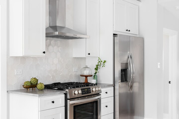 A kitchen detail with white cabinets, stainless steel appliances, tan hexagon tile backsplash, and...