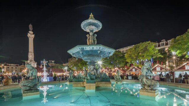 Panorama showing illuminated fountain with evening timelapse view of holiday decorations and food booths at the Rossio Christmas Market on Dom Pedro IV square in Baixa district of Lisbon, Portugal.