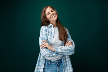 A pretty young woman with brown eyes is wearing a checkered blue shirt and looks confidently at the camera