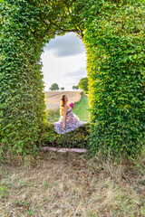 A pregnant woman sits in an arch made of green leaves