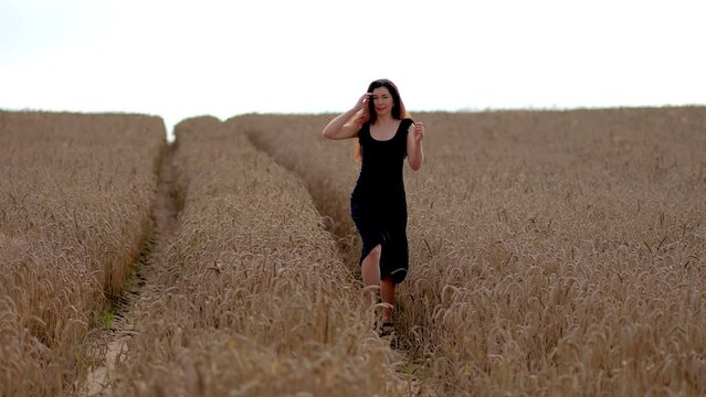 Beautiful slim woman running in wheat golden field. Female enjoying countryside nature in summer. Young girl with beautiful hairs moves across grain crops