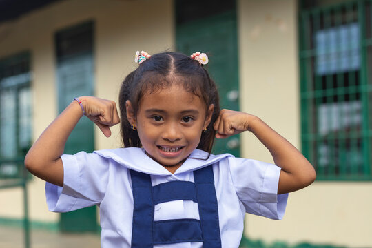 A confident preschooler asian lady flexes her arms. A little girl at a provincial primary school in Bohol.