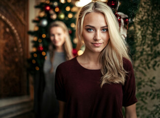 young women standing in front of a christmas tree at home, joyful smile, caucasian blond