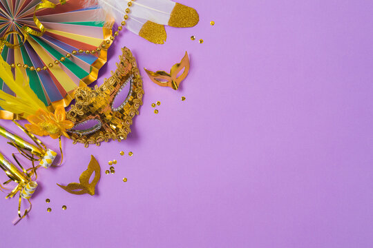 Carnival or mardi gras concept with golden carnival masks and party decorations on purple background. Top view, flat lay