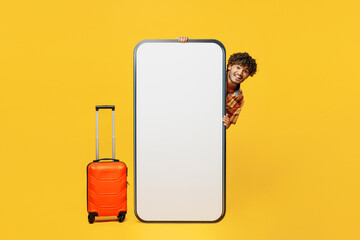 Traveler Indian man wear shirt casual clothes hold bag big huge blank screen mobile cell phone isolated on plain yellow background. Tourist travel abroad in free time rest getaway. Air flight concept.